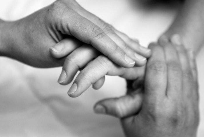 Foto: schwarzweisaufnahme von Händen einer Therapeutin, die die Finger von einer Patientin behandelt
