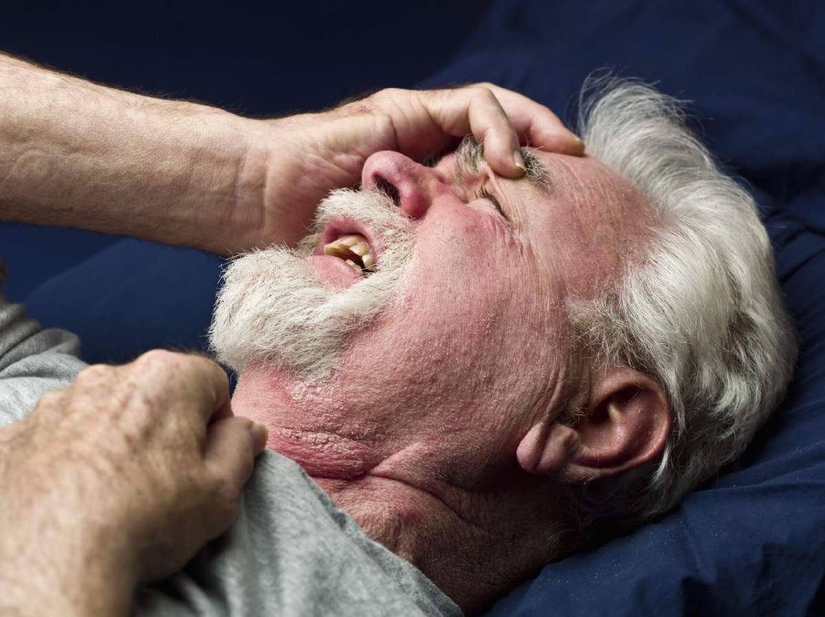 Foto: Ein Mann greift sich liegend und mit schmerzverzerrtem Gesicht an den leicht erhobenen Kopf.
