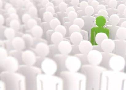 Ein grünes Pappmännchen befindet sich inmitten weißen Pappmännchen und sticht damit aus der Menge heraus